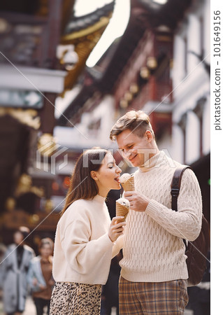 newlywed couple eating ice cream from a cone on a street in Shanghai near Yuyuan. Couple take a break for a snack while visiting China. husband and wife sharing ice cream outisde of a food hall newlywed couple eating ice cream from a cone on a street in Shanghai near Yuyuan. Couple take a break for a snack while visiting China. husband and wife sharing ice cream outisde of a food hall 101649156