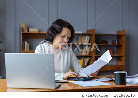 Middle aged senior woman sit with laptop and paper document. Pensive older mature lady reading paper bill pay online at home managing bank finances calculating taxes planning loan debt pension payment Middle aged senior woman sit with laptop and paper document. Pensive older mature lady reading paper bill pay online at home managing bank finances calculating taxes planning loan debt pension payment 101650119