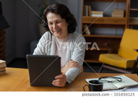 Happy middle aged senior woman holding tablet talk on video call with friends family. Laughing mature old senior grandmother having fun talking speaking with grown up children online Happy middle aged senior woman holding tablet talk on video call with friends family. Laughing mature old senior grandmother having fun talking speaking with grown up children online 101650125
