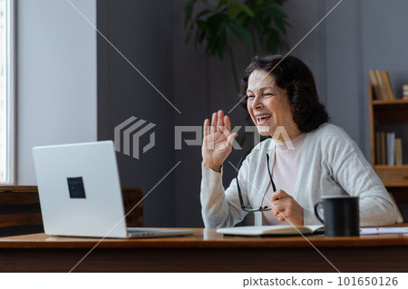 Happy middle aged senior woman sit with laptop talk on video call with friends family. Laughing mature old senior grandmother having fun talking speaking with grown up children online Happy middle aged senior woman sit with laptop talk on video call with friends family. Laughing mature old senior grandmother having fun talking speaking with grown up children online 101650126