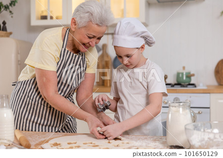 Happy family in kitchen. Grandmother granddaughter child cutting cookies of dough on kitchen table together. Grandma teaching kid girl cook bake cookies. Household teamwork helping family generations 101650129