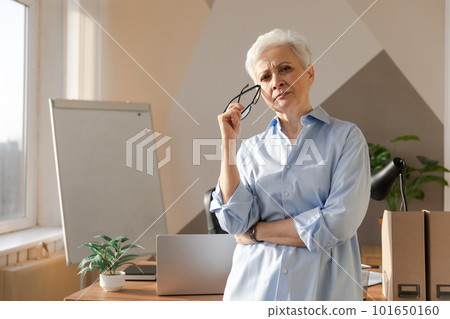 Portrait of confident stylish european middle aged senior woman at workplace. Stylish older mature 60s gray haired lady businesswoman in modern office. Boss leader teacher professional worker Portrait of confident stylish european middle aged senior woman at workplace. Stylish older mature 60s gray haired lady businesswoman in modern office. Boss leader teacher professional worker 101650160