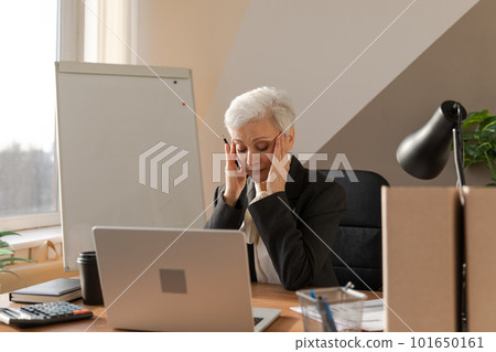 Senior woman touching temples experiencing stress in office. Mature lady tired of working feeling headache sick rubbing temples forehead. Long laptop usage computer vision syndrome. Office syndrome Senior woman touching temples experiencing stress in office. Mature lady tired of working feeling headache sick rubbing temples forehead. Long laptop usage computer vision syndrome. Office syndrome 101650161