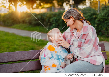 mother and son sit on a park bench in the rays of the setting sun. the concept of a family. Mother's Day. beautiful girl (mother) with a boy (son) in the park in the park are sitting on a bench at 101650859