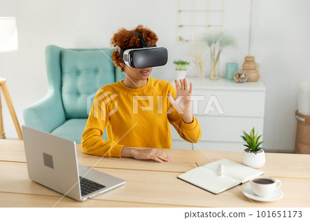 African american young woman wearing using virtual reality metaverse VR glasses headset at home. Girl touching air during VR experience on virtual reality helmet. Simulation hi-tech videogame concept African american young woman wearing using virtual reality metaverse VR glasses headset at home. Girl touching air during VR experience on virtual reality helmet. Simulation hi-tech videogame concept 101651173