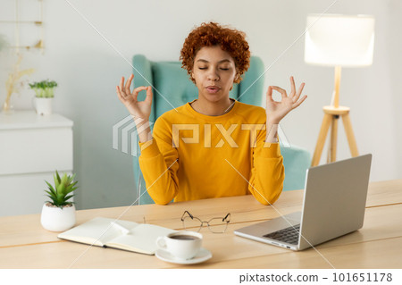 Yoga mindfulness meditation. No stress keep calm. African girl practicing yoga at home office. Woman in lotus pose at office table meditating relaxing indoor. Girl doing breathing practice at work 101651178