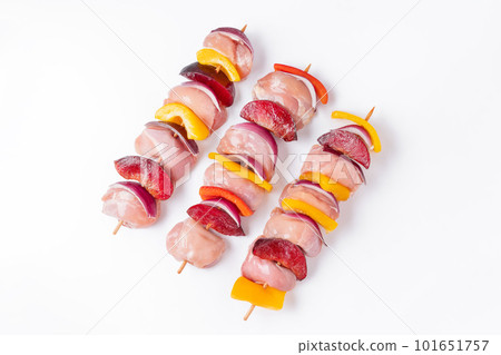 Raw chicken leg meat skewers with vegetables,plums,peppers,onions, on a white background.Uncooked mixed meat skewer with peppers.Skewers with pieces of raw meat, red, yellow and green pepper.Top view. 101651757