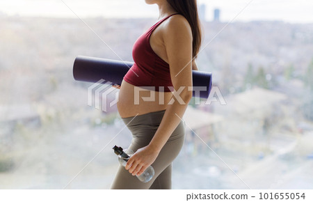 Pregnant woman going to prenatal yoga class showing beautiful baby bump belly holding yoga mat and water bottle in profile. Woman living healthy active pregnancy lifestyle 101655054