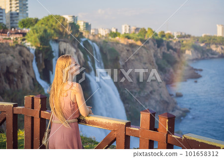 Beautiful woman with long hair on the background of Duden waterfall in Antalya. Famous places of Turkey. Lower Duden Falls drop off a rocky cliff falling from about 40 m into the Mediterranean Sea in 101658312