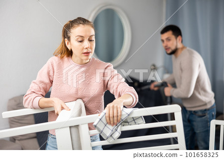Woman rubbing wooden furniture while husband vacuuming Woman rubbing wooden furniture while husband vacuuming 101658325