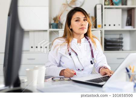 Doctor in uniform is working behind laptop in clinic Doctor in uniform is working behind laptop in clinic 101658500