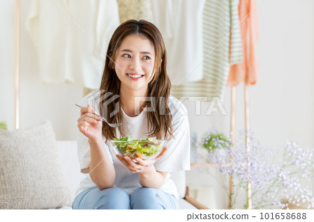 Young woman eating salad in the living room 101658688
