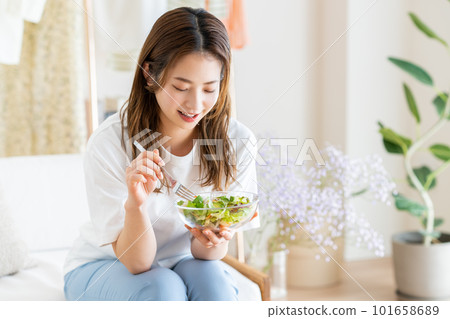 Young woman eating salad in the living room 101658689