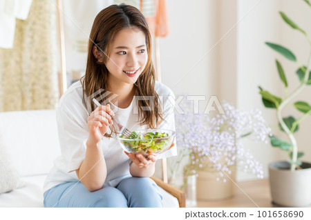 Young woman eating salad in the living room 101658690