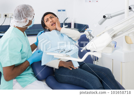 Latina suffering from toothache talking to stomatologist in clinic 101658718