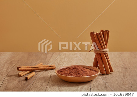 A bunch of cinnamon sticks standing next to a wooden dish of cinnamon powder on a wooden table. cinnamon (Cinnamomum) is useful for cooking and also good for health 101659047