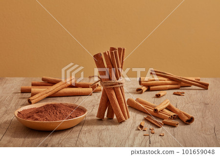 Many cinnamon sticks are decorated on a wooden table with cinnamon powder placed on a dish. Cinnamon (Cinnamomum) brings a lot of benefits for health, body and skin Many cinnamon sticks are decorated on a wooden table with cinnamon powder placed on a dish. Cinnamon (Cinnamomum) brings a lot of benefits for health, body and skin 101659048