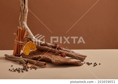 Some tree branches with a bunch of cinnamon sticks, dried orange slices and star anise placed on, many peppers scattered around. Organic herbal concept 101659051