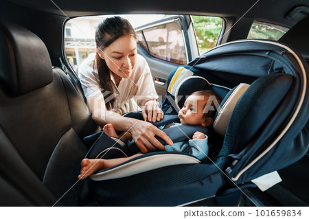happy mother is fastening safety belt to newborn baby in car seat 101659834