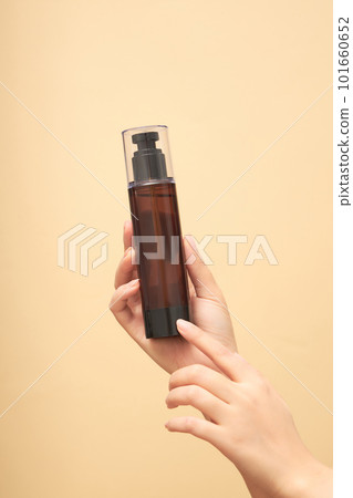 Female hand holding on pointing to an unlabeled bottle on beige background. Minimal concept for advertising cosmetic product with hand model. Front view, space for design. Copy space Female hand holding on pointing to an unlabeled bottle on beige background. Minimal concept for advertising cosmetic product with hand model. Front view, space for design. Copy space 101660652