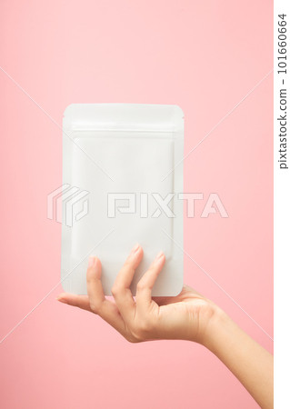 Female hand holding a facial sheet mask white blank realistic mockup on trendy pink background. Space for label design, front view. Daily skincare routine. 101660664
