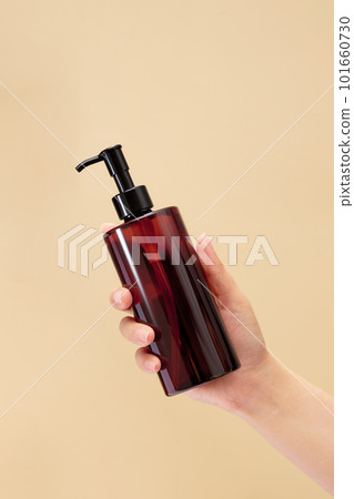 Beautiful female hand is holding a transparent pump bottle dispenser. Organic beauty product concept. Empty label for beauty product mockup 101660730