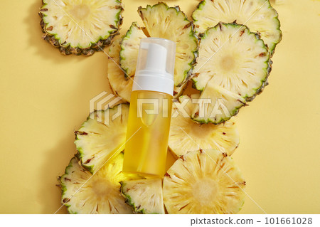 A transparent bottle filled with yellow liquid displayed on a pile of pineapple slices. Product mockup of pineapple (Ananas comosus) extract 101661028