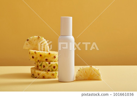 An empty label bottle in white color decorated with pineapple (Ananas comosus) slices on light background. Pineapple has many benefits for skin and hair 101661036