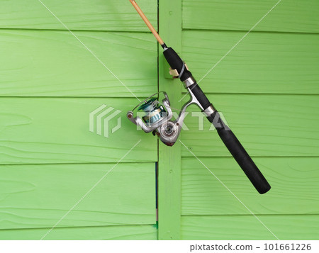 Fishing rod is hung on a green wooden wall. 101661226