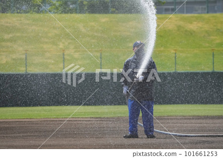 A maintenance worker sprinkling water on a baseball field A maintenance worker sprinkling water on a baseball field 101661253