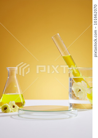 Front view of laboratory equipment filled with yellow liquid in erlenmeyer flask and test tube, white flower in beaker and transparent empty podium on yellow background. Space for display product. Front view of laboratory equipment filled with yellow liquid in erlenmeyer flask and test tube, white flower in beaker and transparent empty podium on yellow background. Space for display product. 101662070