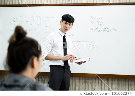 An Asian male teacher in a classroom near the whiteboard is writing and teaching a lesson with a special lecture in a class column. Math teacher explains arithmetic sums to university students An Asian male teacher in a classroom near the whiteboard is writing and teaching a lesson with a special lecture in a class column. Math teacher explains arithmetic sums to university students 101662274
