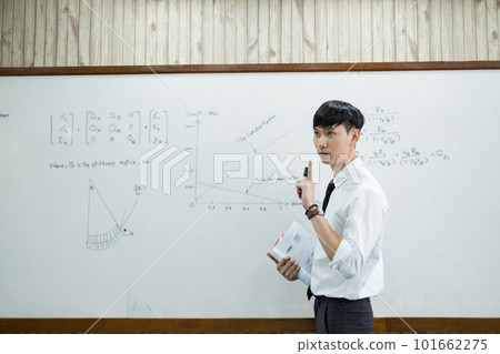 An Asian male teacher in a classroom near the whiteboard is writing and teaching a lesson with a special lecture in a class column. Math teacher explains arithmetic sums to university students An Asian male teacher in a classroom near the whiteboard is writing and teaching a lesson with a special lecture in a class column. Math teacher explains arithmetic sums to university students 101662275