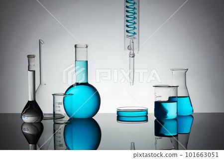 Minimal art background with petri dish, beaker, erlenmeyer flask, boiling flask and lab glassware containing blue liquid on back lit background. 101663051
