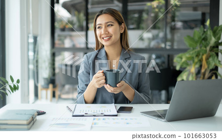 Asian businesswoman smiling happily with a new morning holding a cup of coffee lightly sipping coffee professional woman in size working in the office 101663053