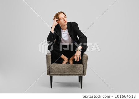 Young barefoot man in black suit sitting in armchair in studio 101664518