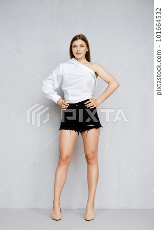 Pretty young woman in black shorts and one sleeve shirt standing with both hands on waist 101664532
