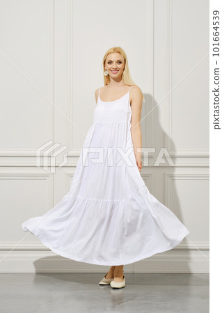 A happy woman in a waving white sundress stands elegantly indoors 101664539