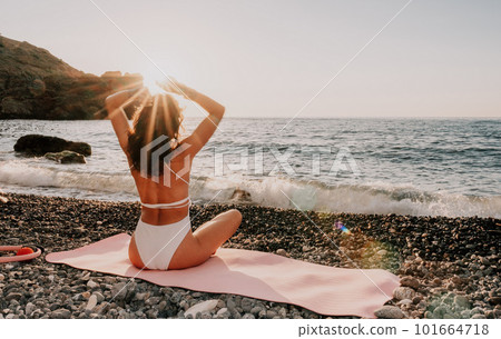 Woman sea yoga. Happy woman in white swimsuit and boho style braclets practicing outdoors on yoga mat by sea on sunset. Women yoga fitness routine. Healthy lifestyle, harmony and meditation Woman sea yoga. Happy woman in white swimsuit and boho style braclets practicing outdoors on yoga mat by sea on sunset. Women yoga fitness routine. Healthy lifestyle, harmony and meditation 101664718