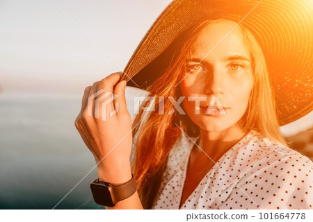 Portrait of happy young woman wearing summer black hat with large brim at beach on sunset. Closeup face of attractive girl with black straw hat. Happy young woman smiling and looking at camera at sea. Portrait of happy young woman wearing summer black hat with large brim at beach on sunset. Closeup face of attractive girl with black straw hat. Happy young woman smiling and looking at camera at sea. 101664778