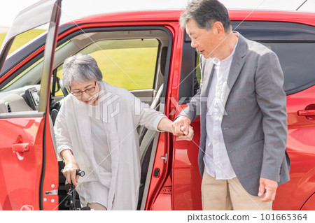 一位拄著拐杖的老婦人從汽車的乘客座位上下來，還有一個幫忙的男人 101665364