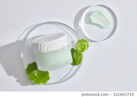 An empty label jar placed on glass transparent podium with gotu kola leaves and cream texture. Product mockup of Gotu kola (Centella asiatica) extract 101665719