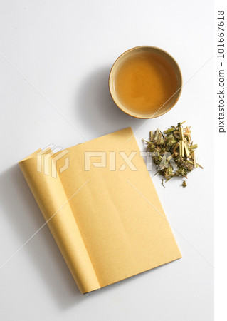 Top view of medicine cup, blank book page and herba leonuri on light background. This is a traditional medicine that has the effect of regulating menstruation and other gynecological diseases. 101667618