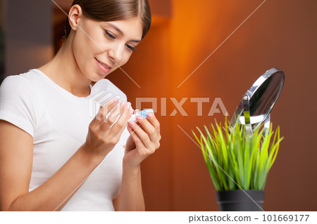 A young woman is putting on contact lenses in front of the mirror. 101669177
