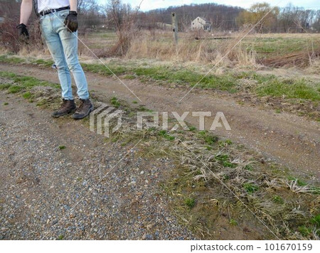 Young farm worker in work gloves and boots stands on a dirt farm road 101670159