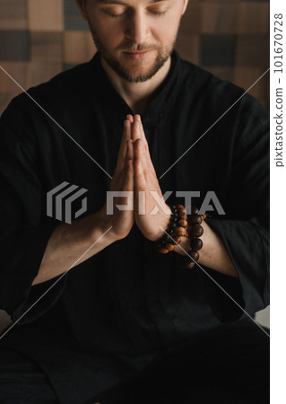 Portrait of a young man in a black kimano sitting in a lotus position on a gym mat in the interior 101670728