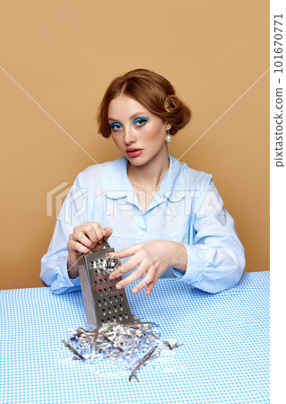 Beautiful young girl with makeup and hairdo grating disco ball on grater over light brown background. Party preparation 101670771