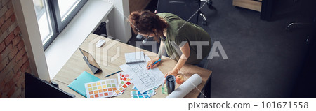 High angle view of interior designer or architect in casual wear with messy hairdo working with color samples and blueprint for new project, standing in her office 101671558