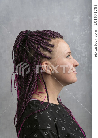 Informal freaky girl wears dreadlocks. Portrait in profile of young woman with pigtails, gray background. Vertical frame 101671783