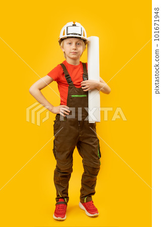 Young boy in protective helmet, overalls and with roll of paper in his hands. Child as builder or architect. Vertical frame. 101671948